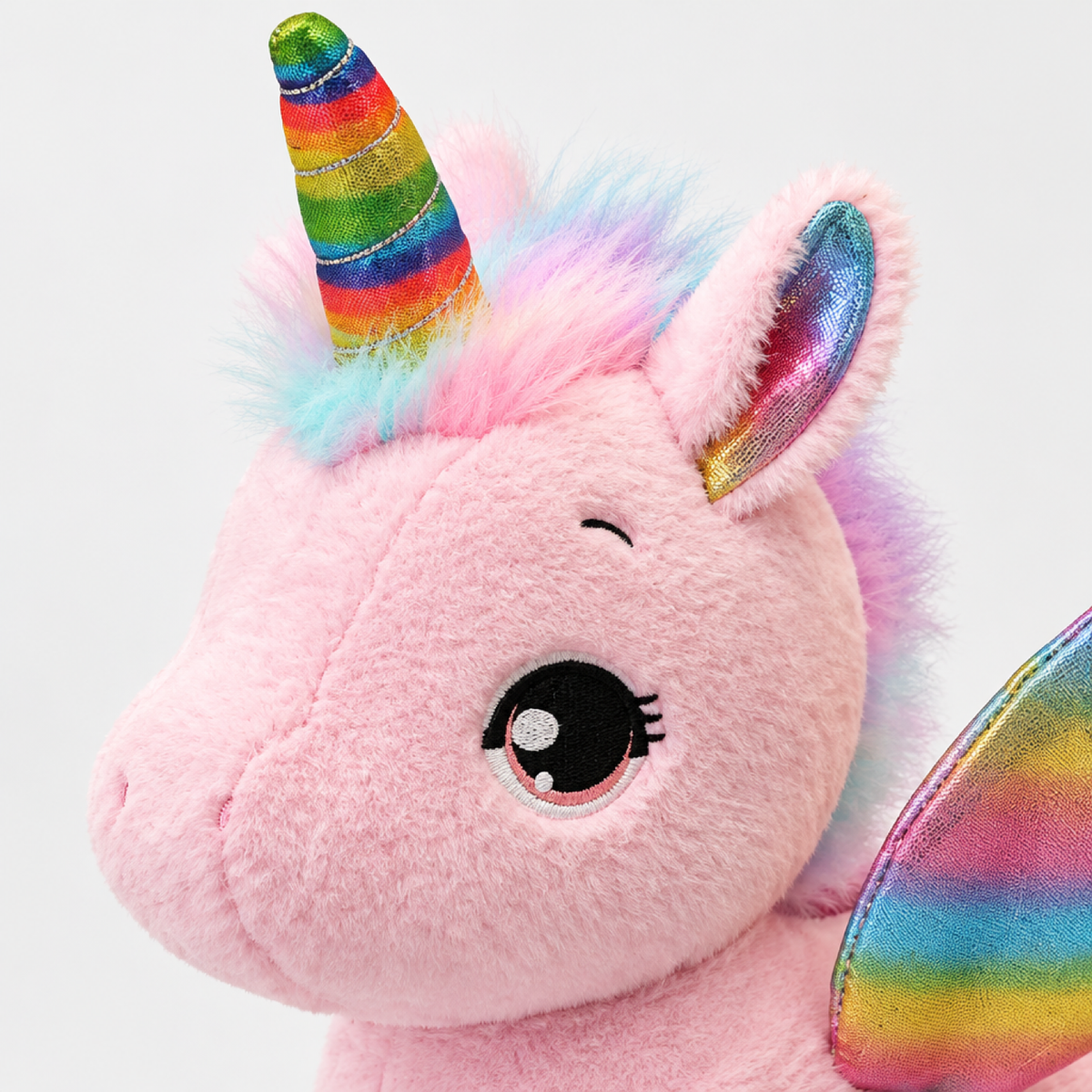 Gros plan du visage de la peluche licorne rose montrant les yeux brodés et le détail de la corne arc-en-ciel