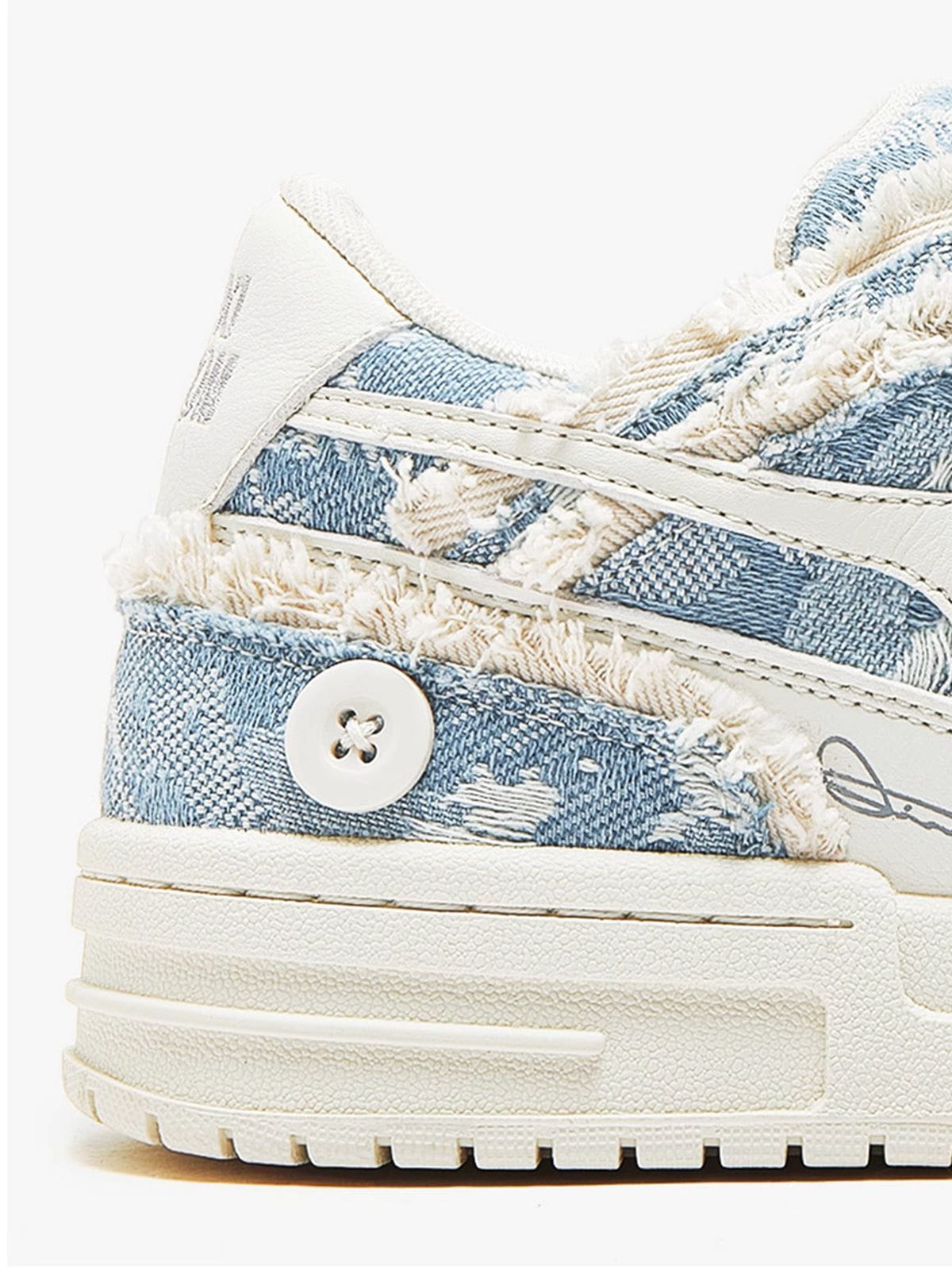 Gros plan du talon de la basket bleue : denim effiloché, bouton décoratif et semelle crantée