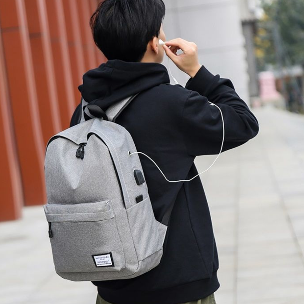 Jeune homme portant le sac à dos ordinateur gris avec écouteurs branchés