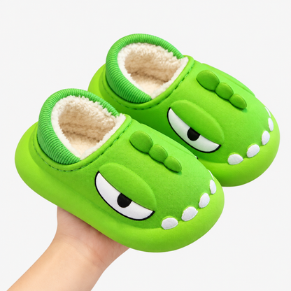 Chausson dinosaure vert clair en coton tenu en main, fond studio blanc
