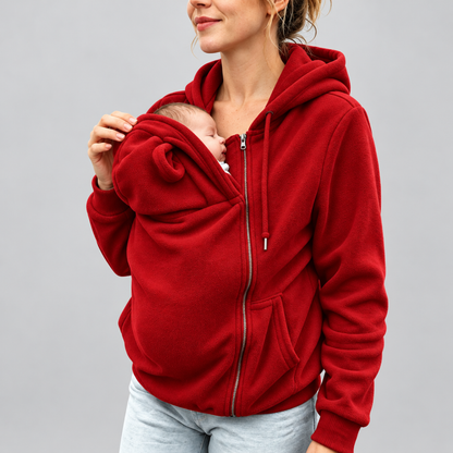 Femme portant le sweat de portage kangourou polaire rouge, poche zippée ouverte avec un nouveau-né installé à l'intérieur