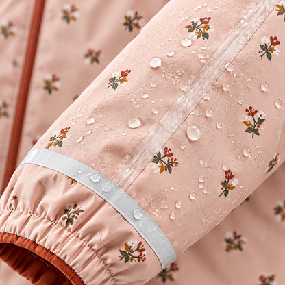 Gros plan sur le tissu imperméable à imprimé floral rose et la couture thermosoudée, avec des gouttes d'eau perlant à la surface