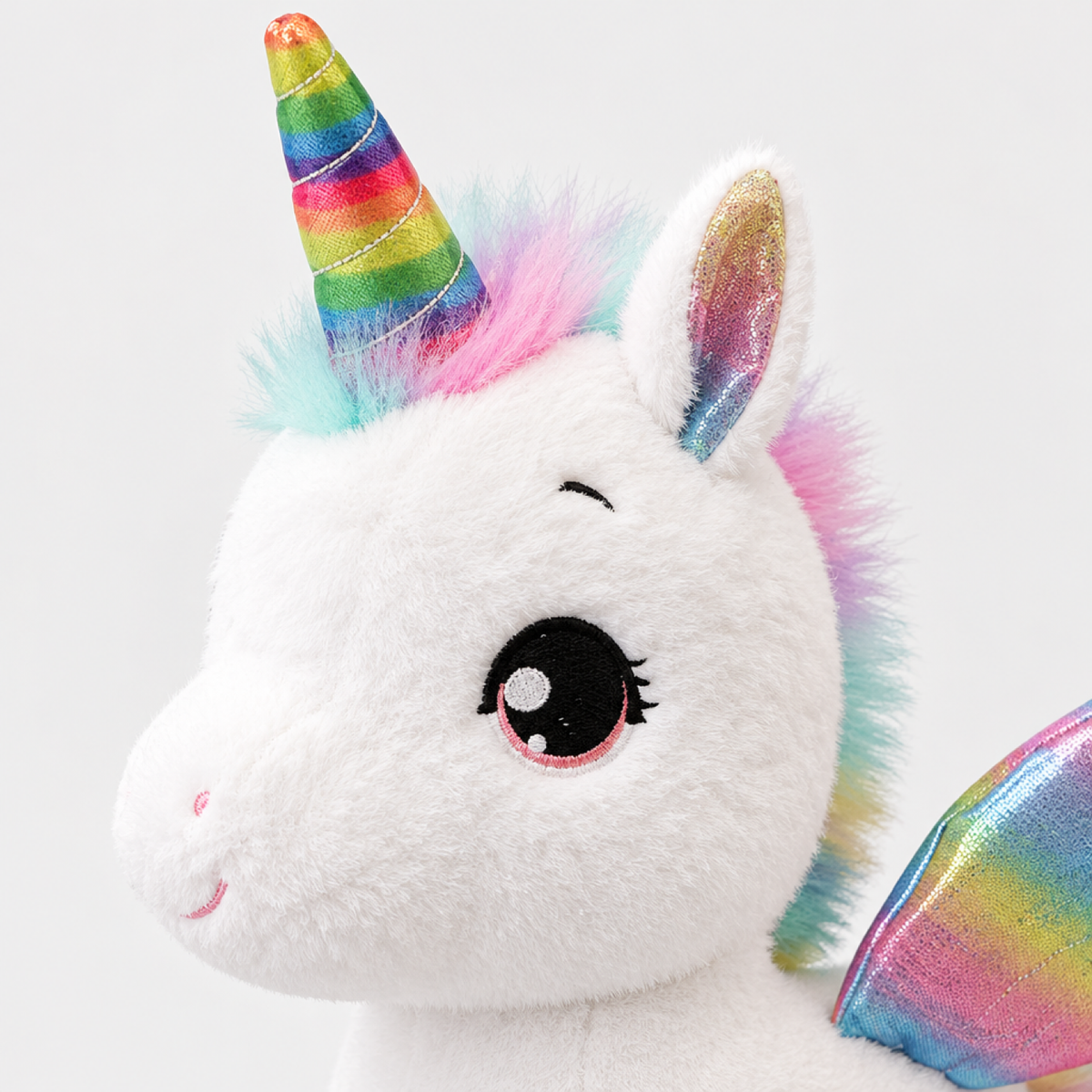 Gros plan du visage de la peluche licorne blanche montrant les yeux brodés et le détail de la corne arc-en-ciel