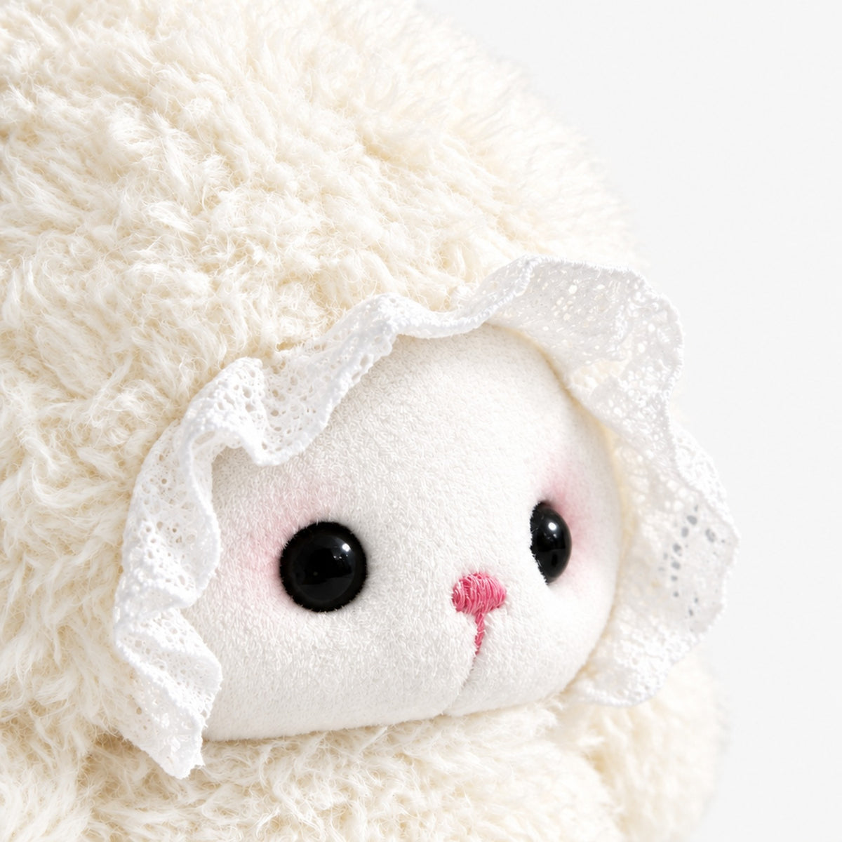 Gros plan sur le visage brodé et le bonnet en dentelle de la peluche agneau