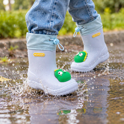 Enfant portant des bottes de pluie imprimé dinosaure en train de sauter dans une flaque d'eau