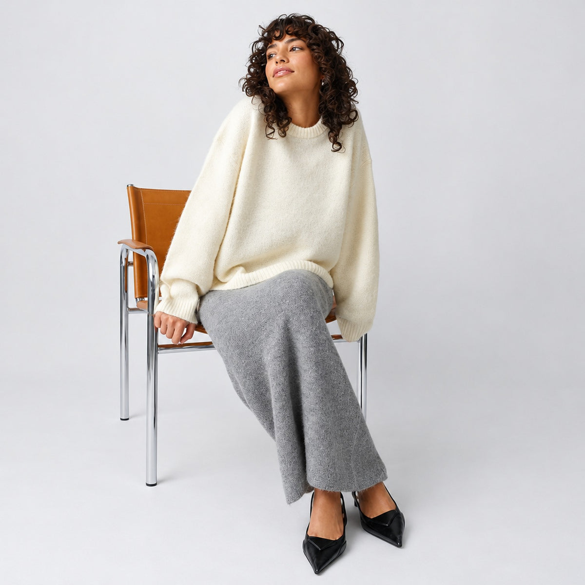 Pull oversize crème porté avec une jupe longue grise et des escarpins noirs