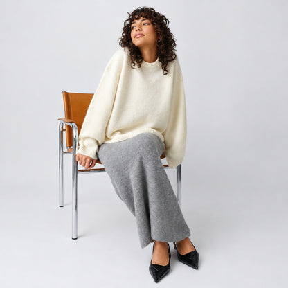 Pull oversize crème porté avec une jupe longue grise et des escarpins noirs