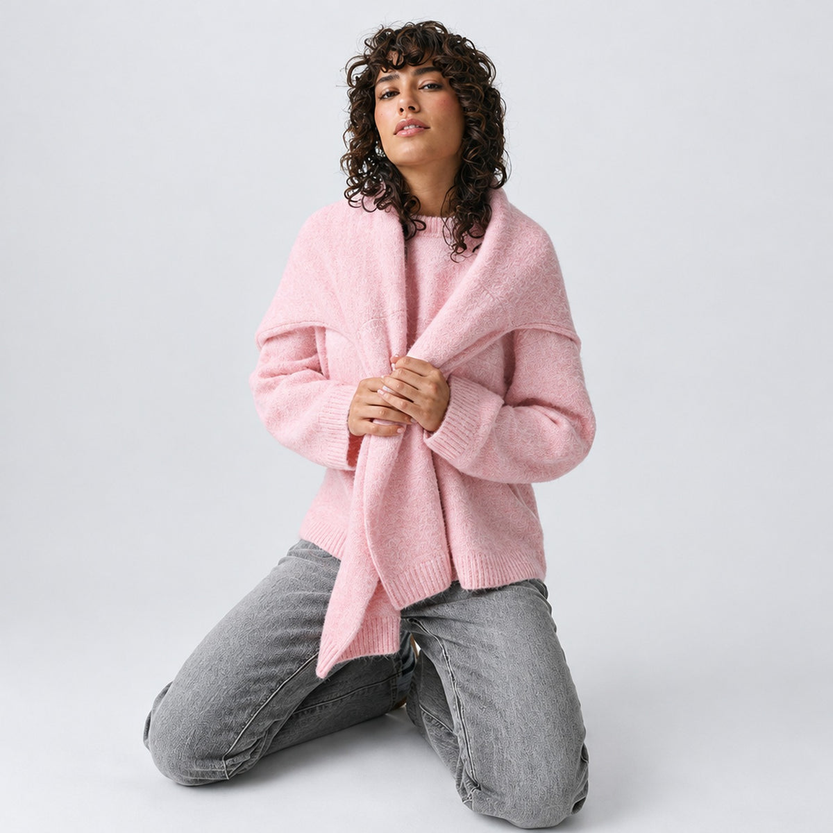 Pull oversize rose porté noué sur les épaules avec un jean gris