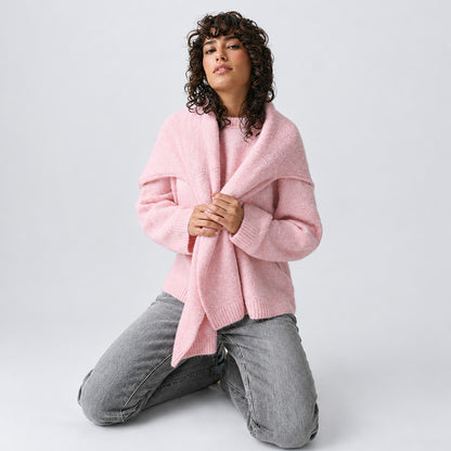 Pull oversize rose porté noué sur les épaules avec un jean gris