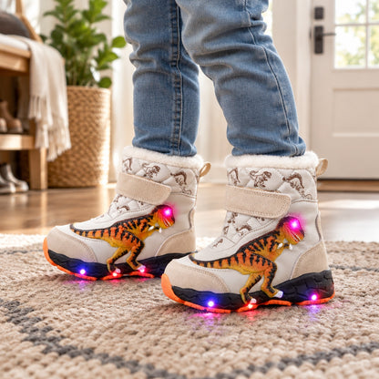 Enfant portant les bottes de neige lumineuses beiges motif dinosaure à l'intérieur, dans l'entrée de la maison